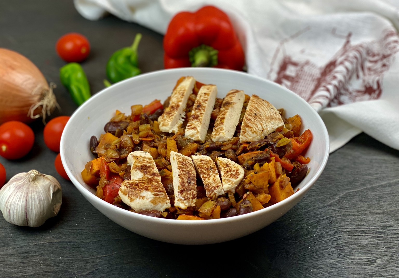 Bowl of chunky pumpkin chili with kidney beans and red peppers, topped with sliced seared chicken breast
