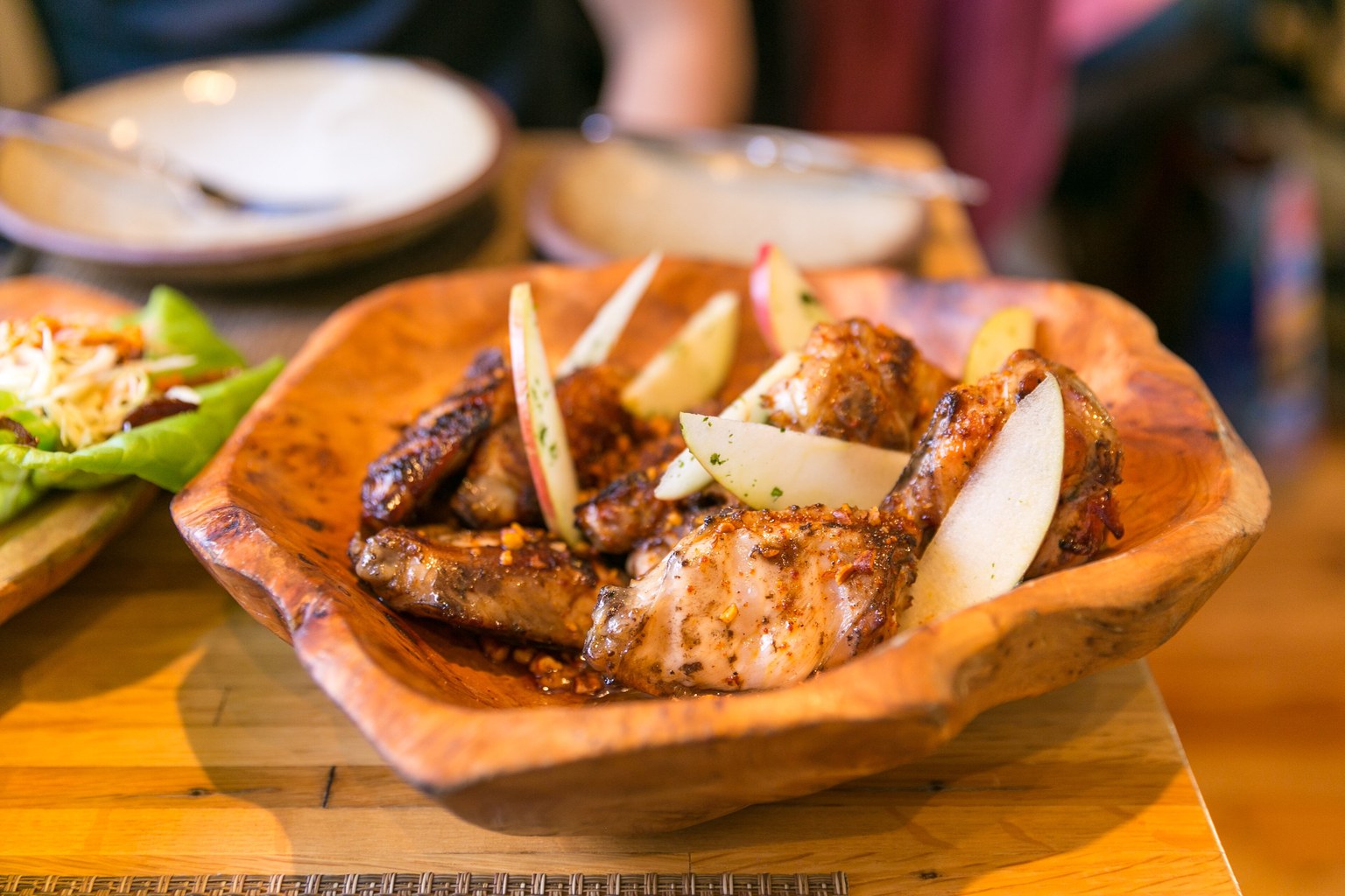 Glossy hot honey glazed chicken wings with chili flakes, chopped pecans and crisp apple slices in a wooden bowl