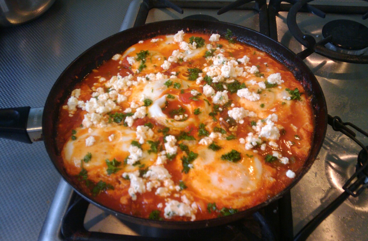 Shakshuka in a black skillet: eggs set in red pepper tomato sauce, topped with crumbled feta and parsley